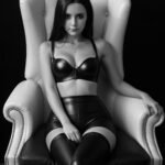 Une femme en cuir assise sur une chaise regarde du sexe anal sur pornhub